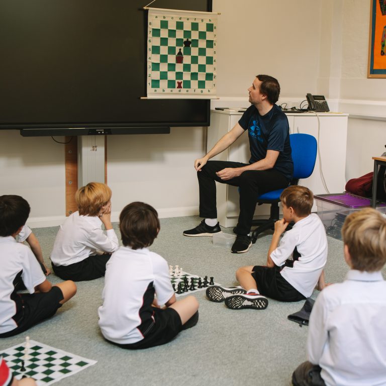 students playing chess on the floor, listening to the teacher